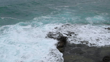 waves crashing into a rocky formation near the shoreline of a large wave breaking on stones to the sides captured at normal speed at 24fps