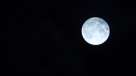 Full-moon-glowing-with-clouds-moving-past-blown-by-wind,-black-background,-night