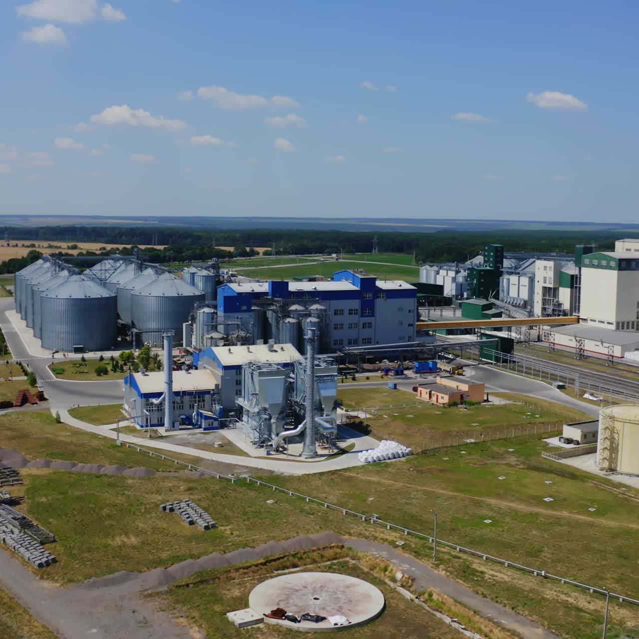 Modern plant on field. Silver silos on agro-processing and manufacturing plant for processing drying cleaning and storage of agricultural products. Aerial view.