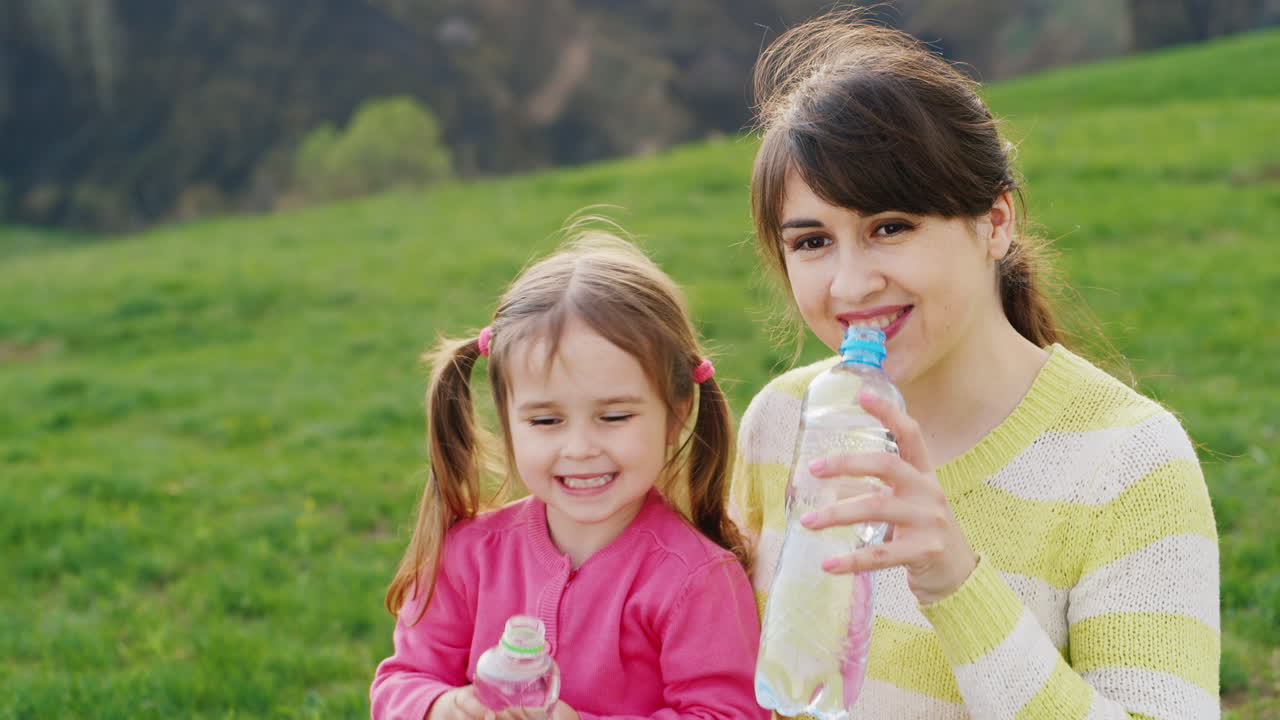 젊은 예쁜 여자가 어린 딸과 함께 플라스틱 병에서 깨끗한 물을 마신다