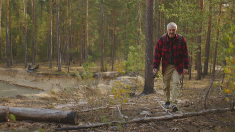 middle-aged traveler with rod and backpack is walking in forest at autumn day resting at nature alone