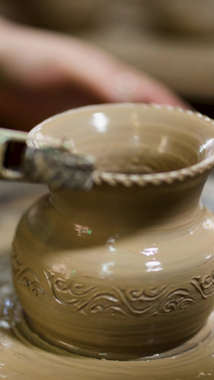 Primo piano di un artigiano che applica motivi intricati a un vaso di argilla in rotazione in Thailandia