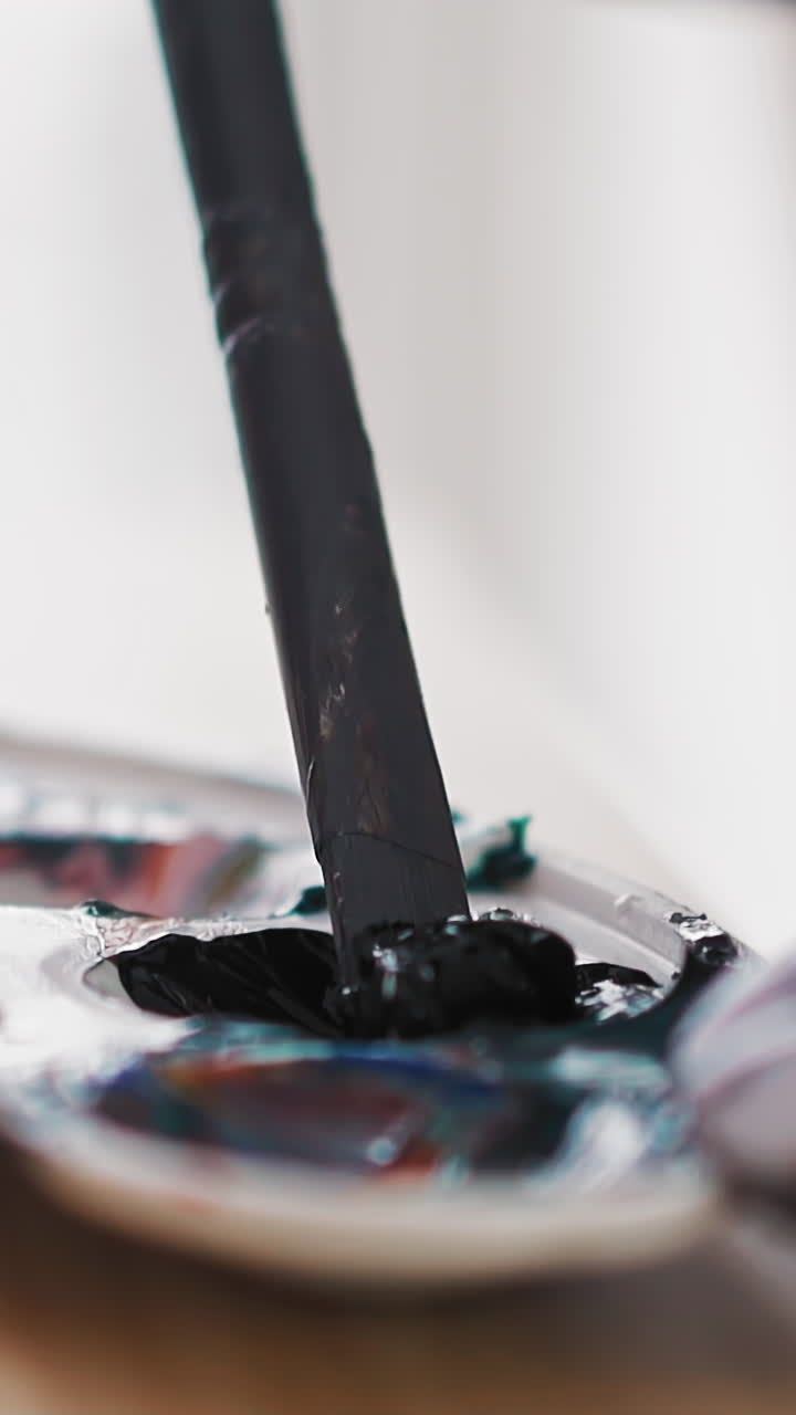 Skilled female artist mixes dark blue paint in cup of white palette with paintbrush at modern wooden easel in studio extreme closeup slow motion
