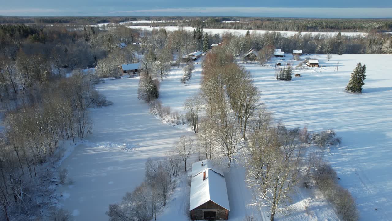 Aerial view of a serene winter countryside featuring snow-covered trees, wooden houses, and a winding road through a frosty forest.