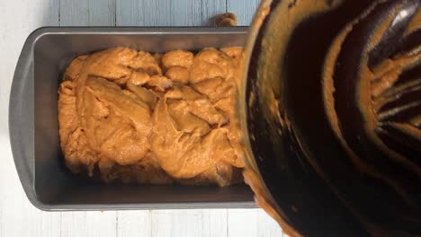 top view of hands scooping pumpkin batter from mixing bowl to loaf pan