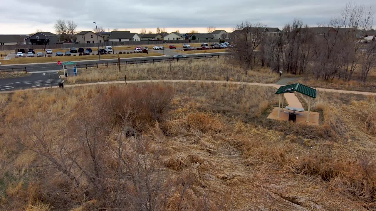 A flight through a gazebo over a picnic table to reveal the neighborhood and location of the park. Suburban Greeley Colorado in winter.
