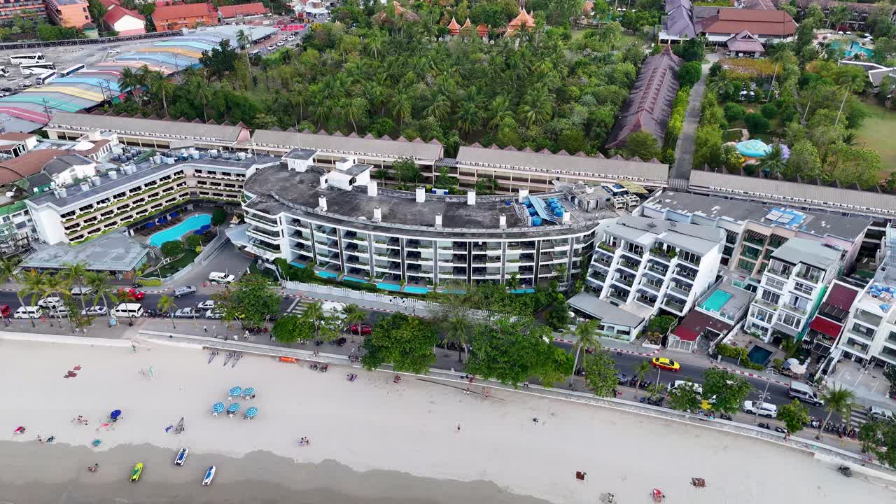 Aerial footage captures the vibrant beachfront of Patong, Phuket, showcasing resorts, shops, and longtail boats along the shore