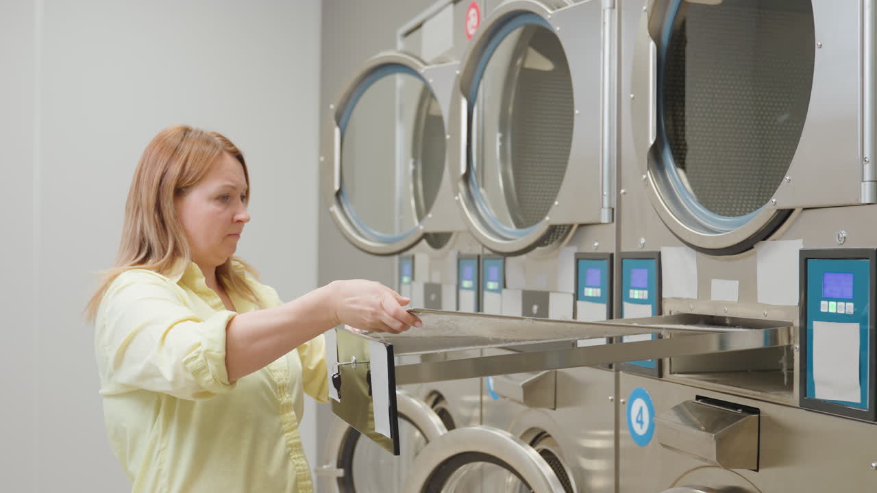 Laundry business owner pushes industrial washing machine filter drawer back into compartment, securing it with key after cleaning, ensuring proper maintenance of equipment in laundromat
