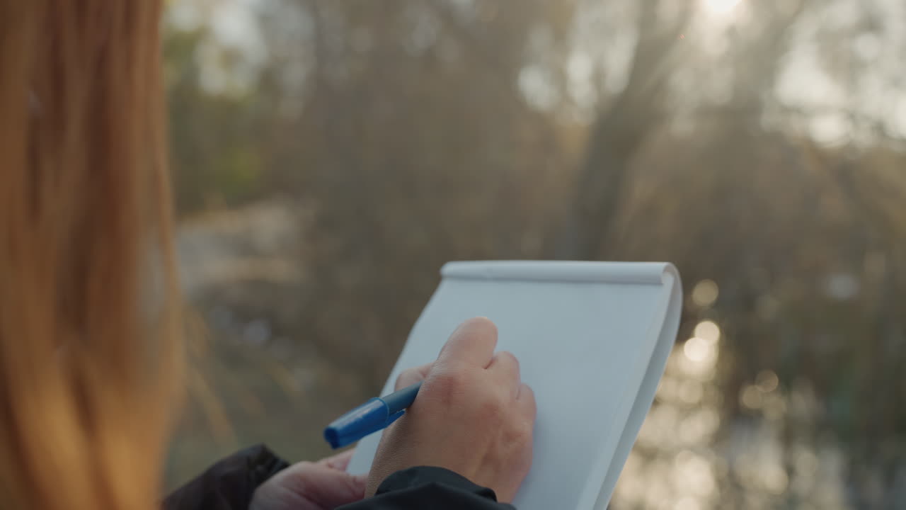 Woman notes outdoors. Caucasian woman documenting details during field study along riverbank. Female scientist making careful notes while exploring scenic trail by shimmering water source