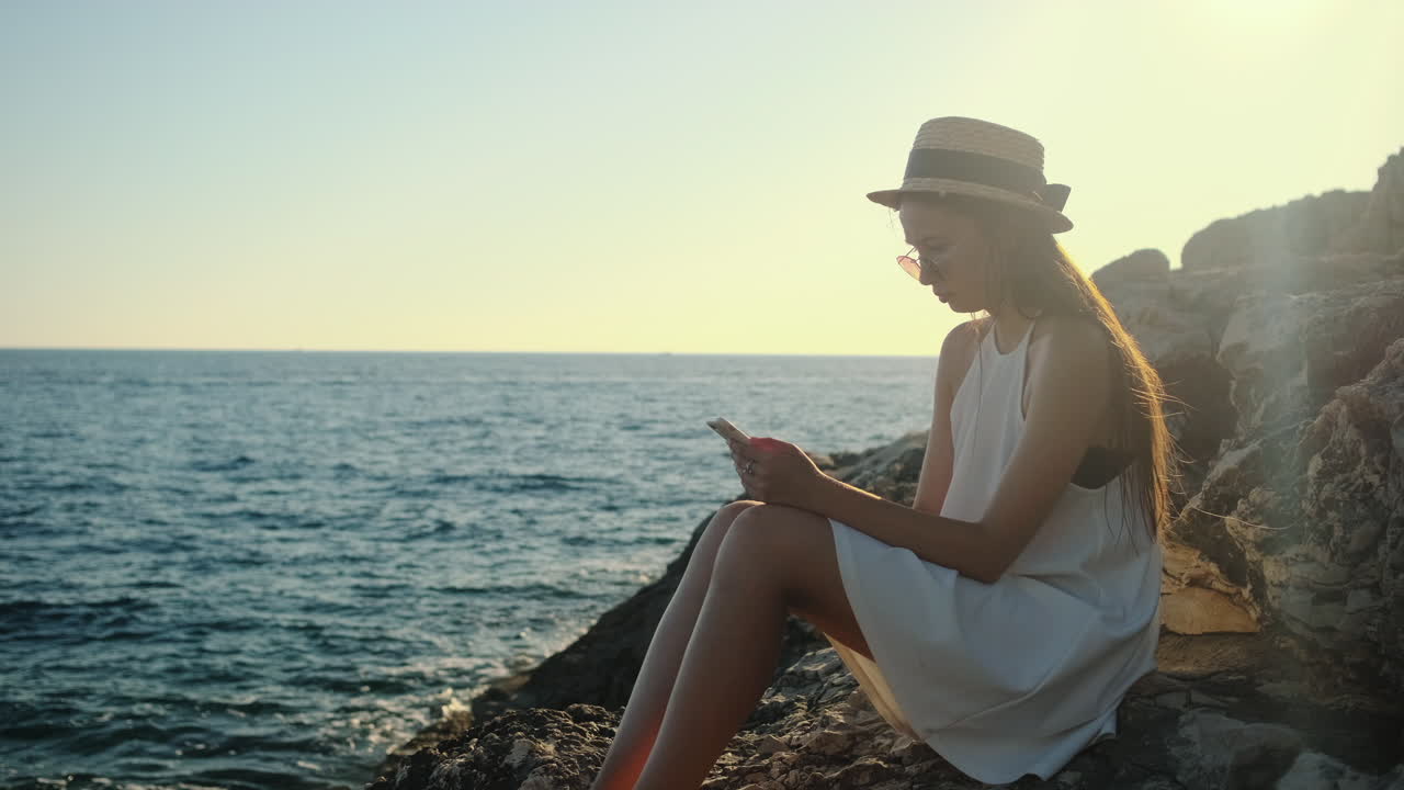 해가 지면 바다 의 바위 위에 앉아 있는 여자