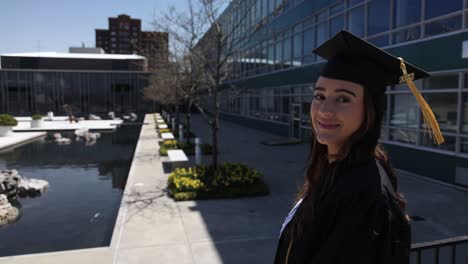 caucasian female college graduate in cap and gown outside turning to camera and smiling in slow motion video