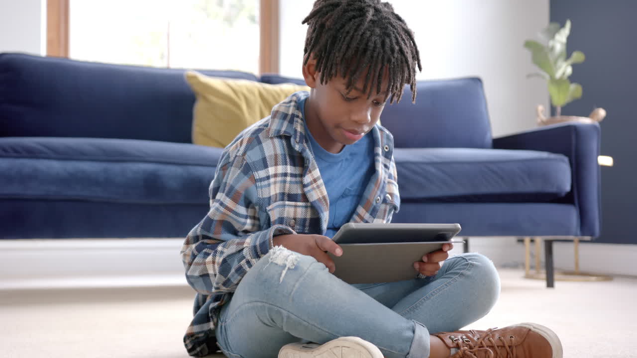 African american boy using tablet sitting on floor at home, slow motion
