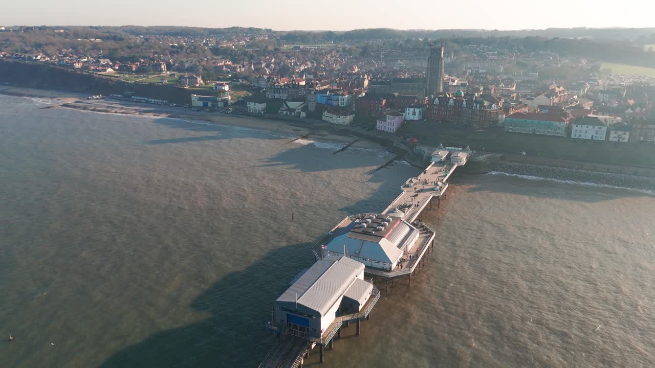 Cromer Pier extending into the sea with a coastal town in the background at sunset