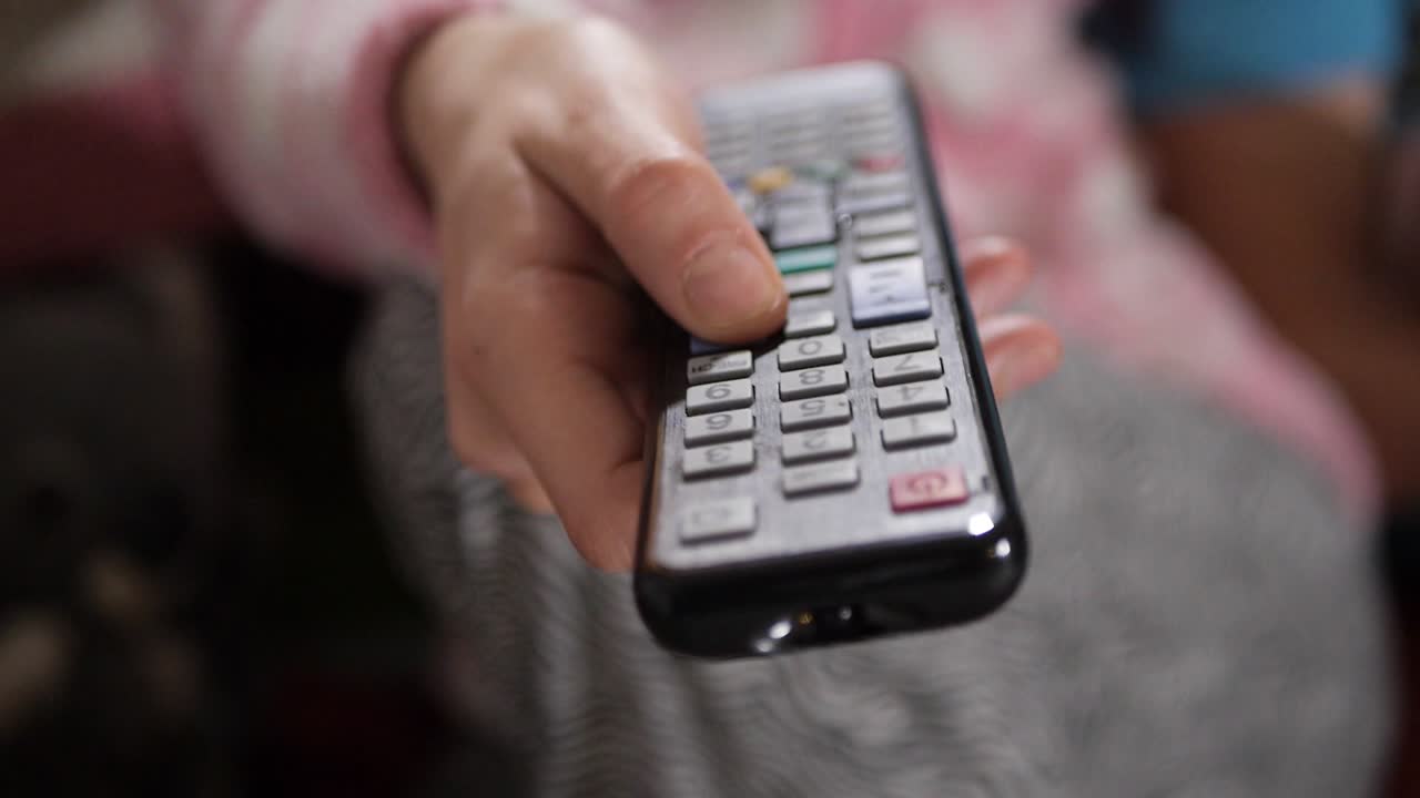 Close up shot of a female hand holding the TV remote control and changing television channels.