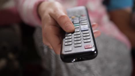 close up shot of a female hand holding the tv remote control and changing television channels.