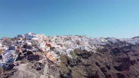 Drone-view-over-Santorini,-aerial-view-over-the-whitewashed-village-of-Oia-with-luxury-vacation-resort