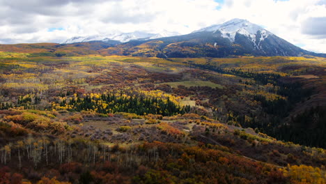 Dramatic-sunny-cloudy-autumn-Aspen-Tree-fall-colors-Kebler-Pass-aerial-cinematic-drone-snow-on-peaks-landscape-Crested-Butte-Gunnison-Colorado-fall-red-yellow-orange-Rocky-Mountains-forward-reveal