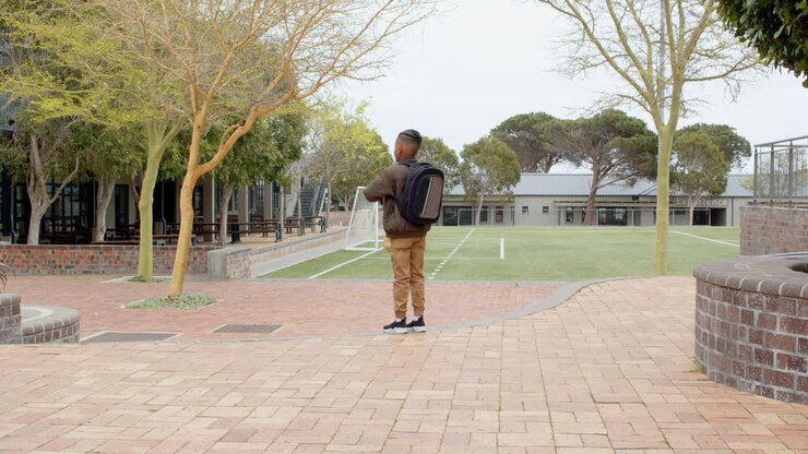Multiracial boys running joyfully with backpacks and lunch bags on school campus