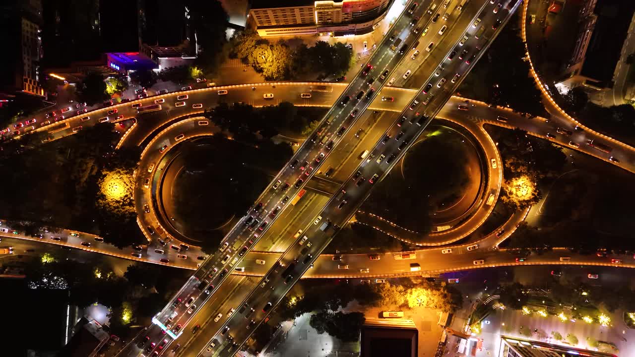 Aerial view of a busy traffic interchange in Guangzhou, China, at night. The illuminated roads and circular lanes capture the energy of rush hour in this bustling urban setting. UHD.