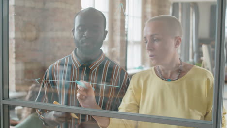 multiethnic colleagues drawing graph on glass wall and speaking