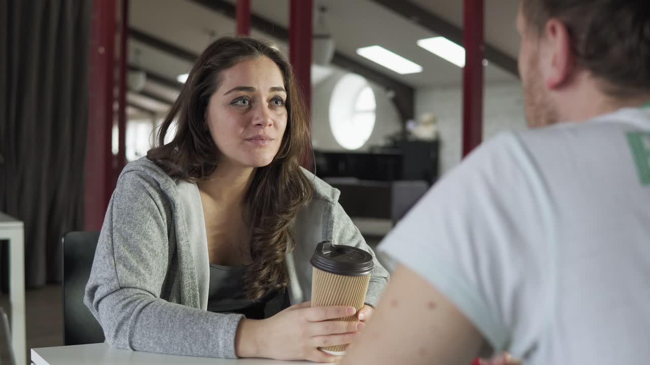 dos amigos están sentados en la mesa en una cafetería, bebiendo café para llevar en vasos de papel y hablando. filmado en 4k