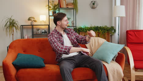 man singing dancing celebrate victory win enjoying music sitting on couch in living home room