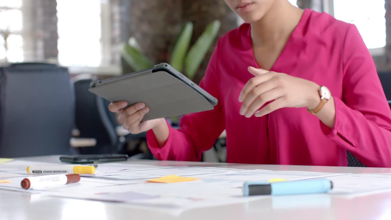 mujer de negocios casual biracial usando una tableta y comprobando documentos en cámara lenta