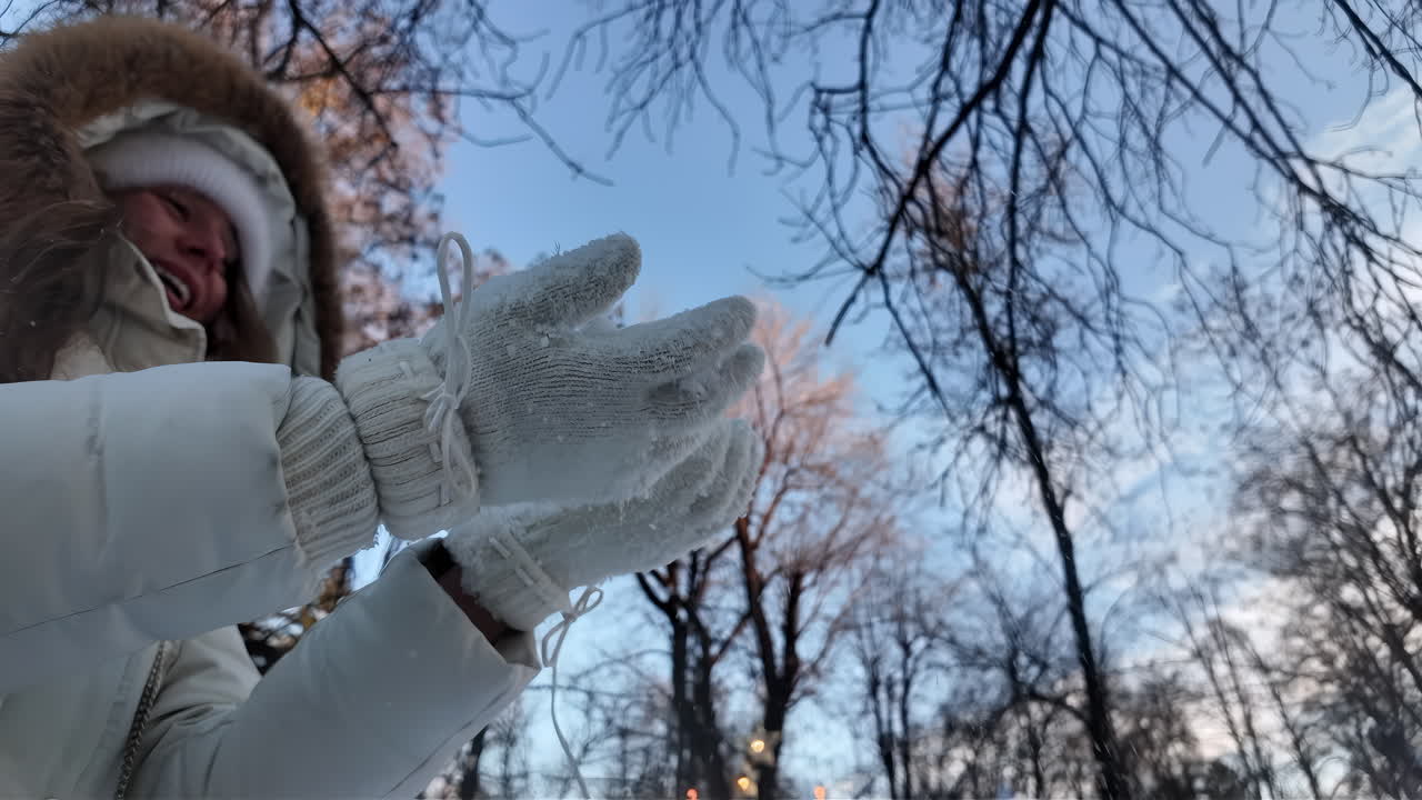 Woman having fun in winter throwing white snow in the air and smiling, slow motion
