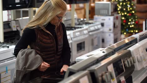 primer plano de una mujer rubia bastante madura comprando una estufa en una sala de exposición de una tienda de electrodomésticos de cocina