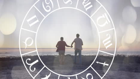 animation of horoscope moving over happy biracial couple holding hands at beach