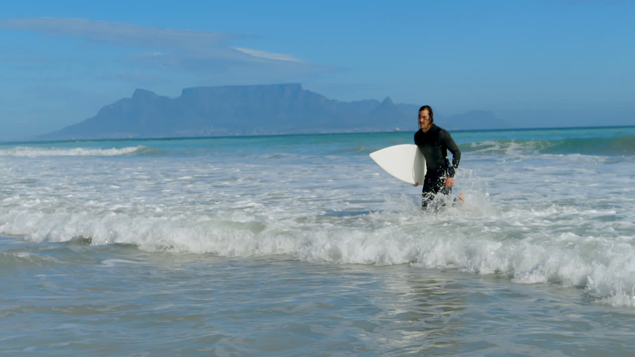 hombre con tabla de surf corriendo en el mar 4k
