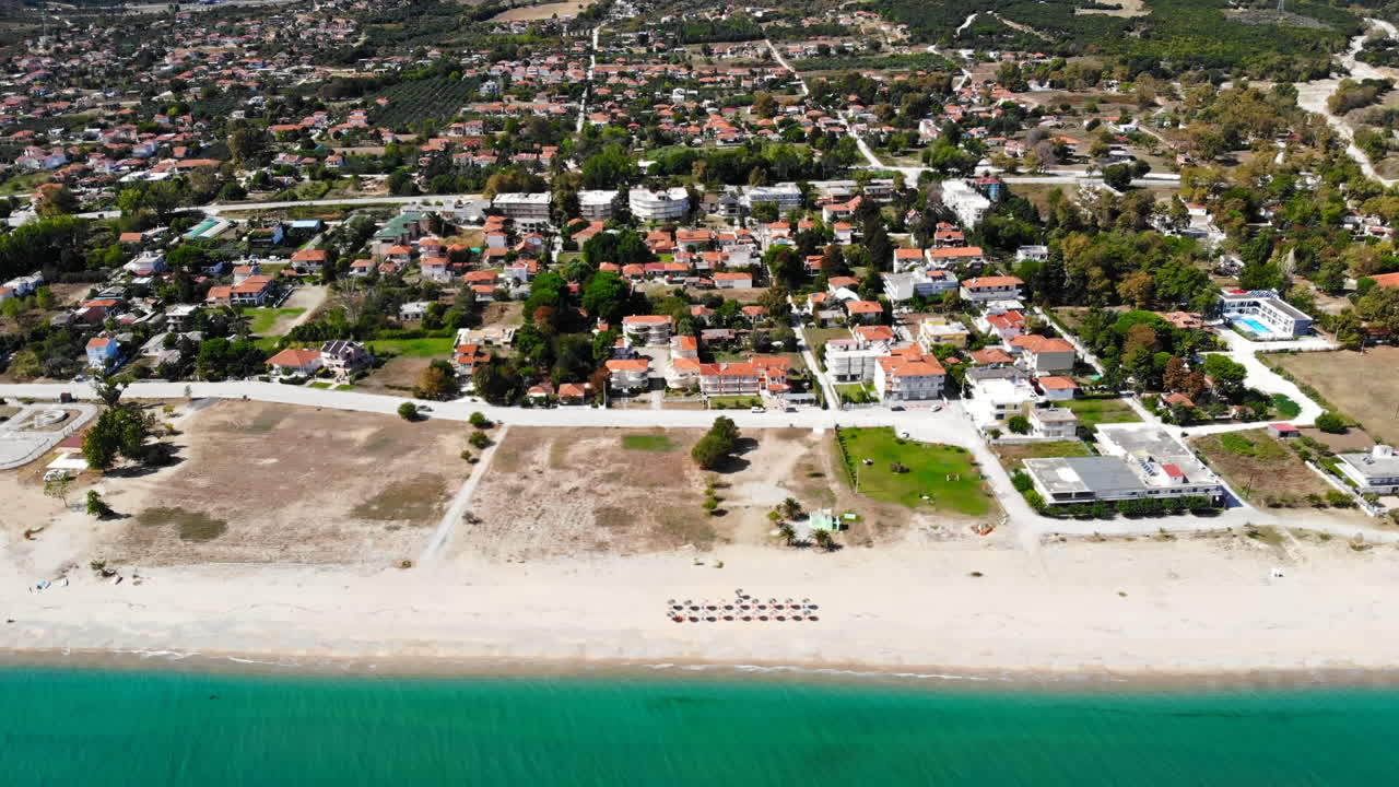 Asprovalta with multiple buildings and greenery, green hills on the background. Aegean sea coast. Long beach along the town. Sunny day. Greece