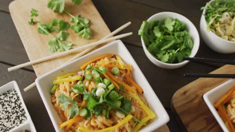 composition of bowls with pad thai, vegetables, sauces and spices on wooden background