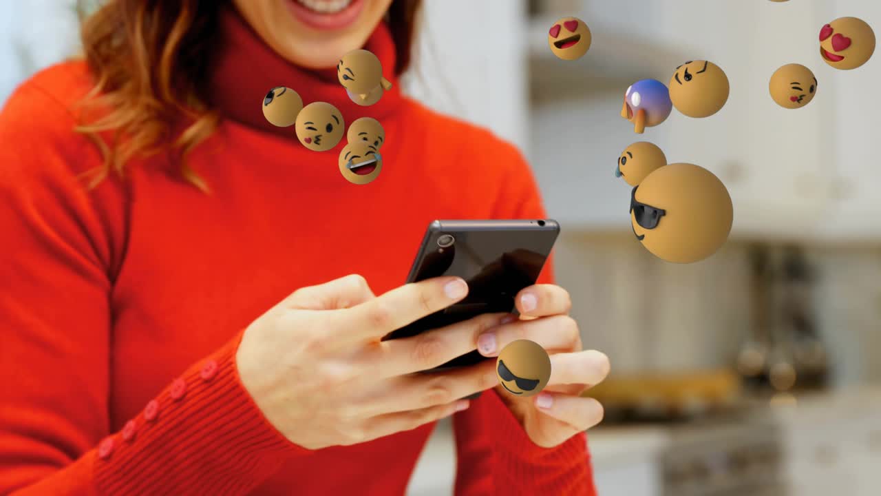 Woman tapping smartphone, activating floating emoticon spheres around laptop for technology demo