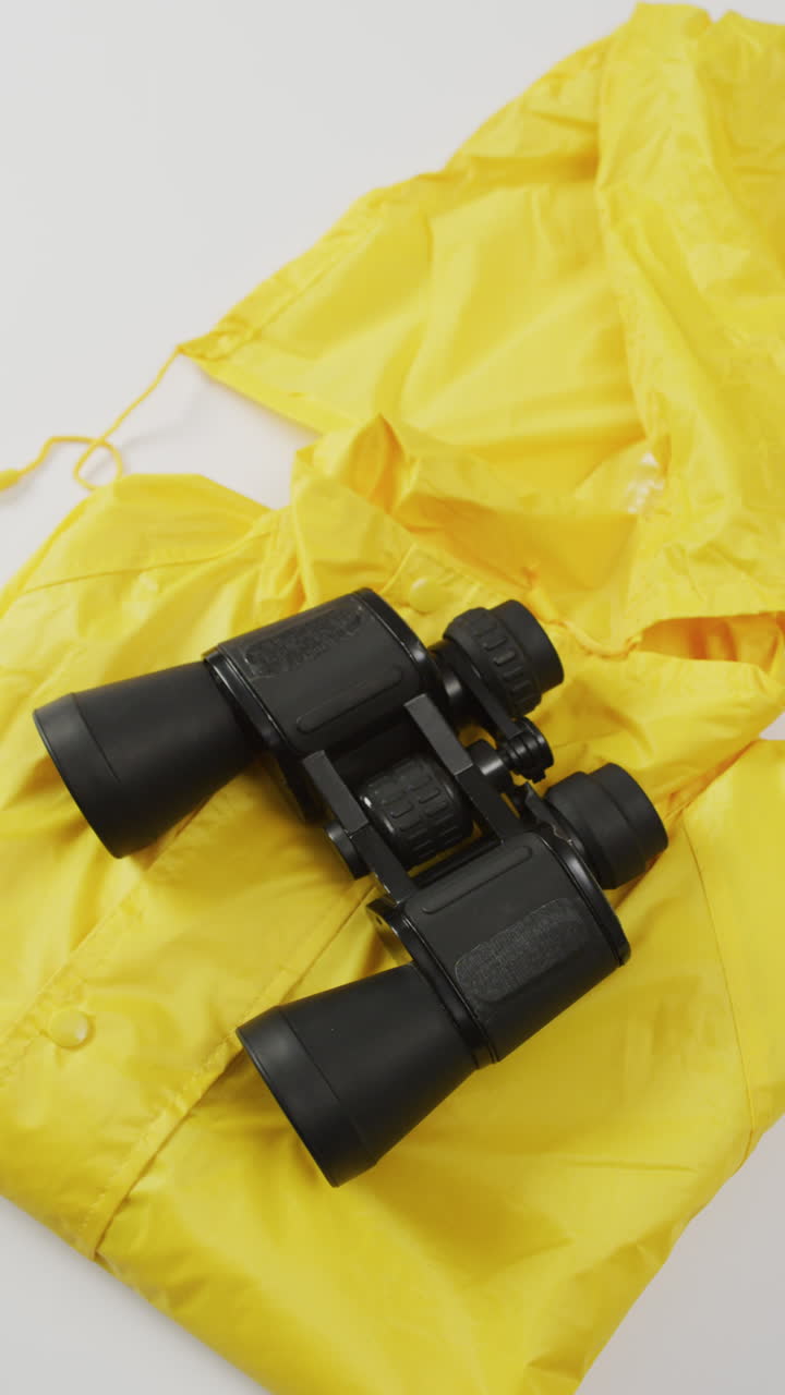 Vertical video of camping equipment with binoculars and yellow rain jacket and copy space