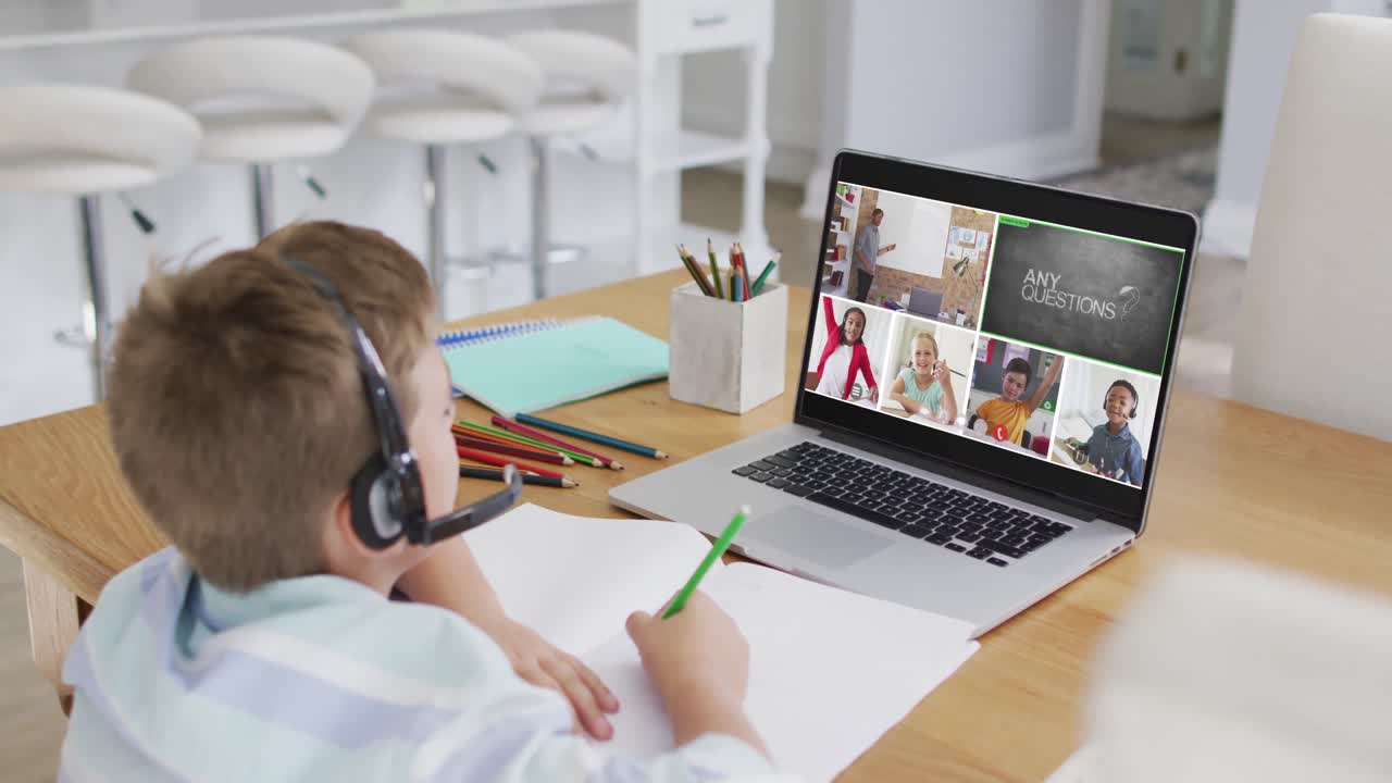 Schoolboy using laptop for online lesson at home, with diverse teacher and class on screen