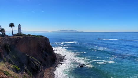 Small-boat-riding-in-the-Pacific-ocean-in-Rancho-Palos-Verdes-with-a-lighthouse-and-Catalina-island-in-the-background