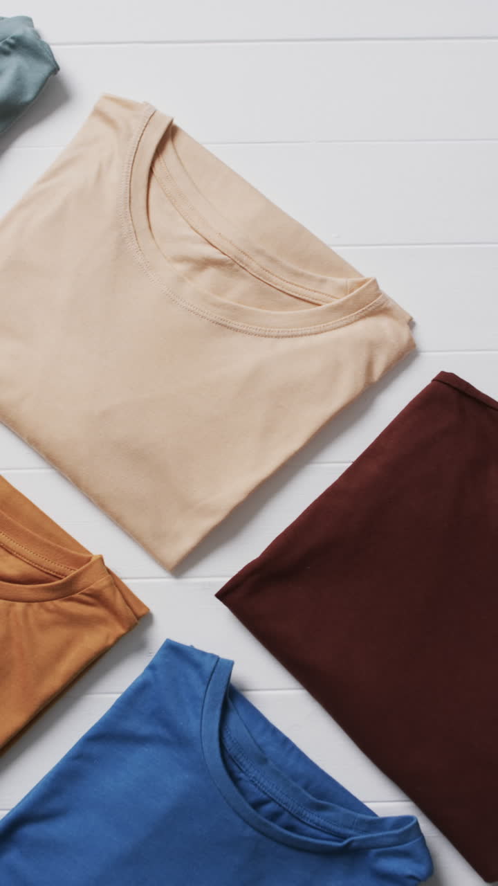Vertical video of multi coloured t shirts with copy space on white background