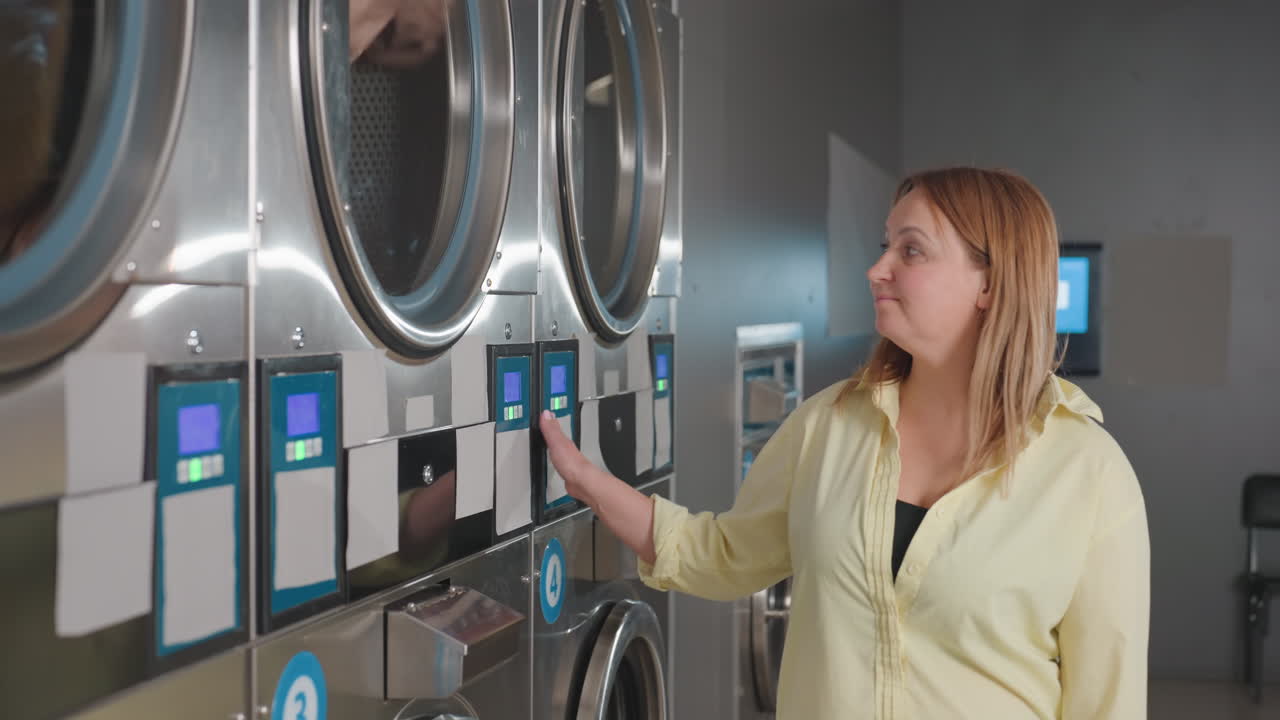 Smiling laundry owner glides hand across industrial washer while clothes tumble inside, digital controls glowing, stainless drums humming in modern laundromat, showcasing service, cleanliness