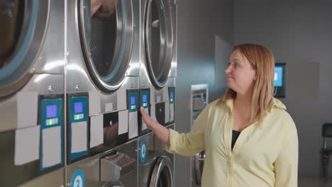 smiling laundry owner glides hand across industrial washer while clothes tumble inside, digital controls glowing, stainless drums humming in modern laundromat, showcasing service, cleanliness