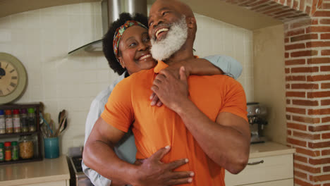 african american senior couple embracing each other in the kitchen at home