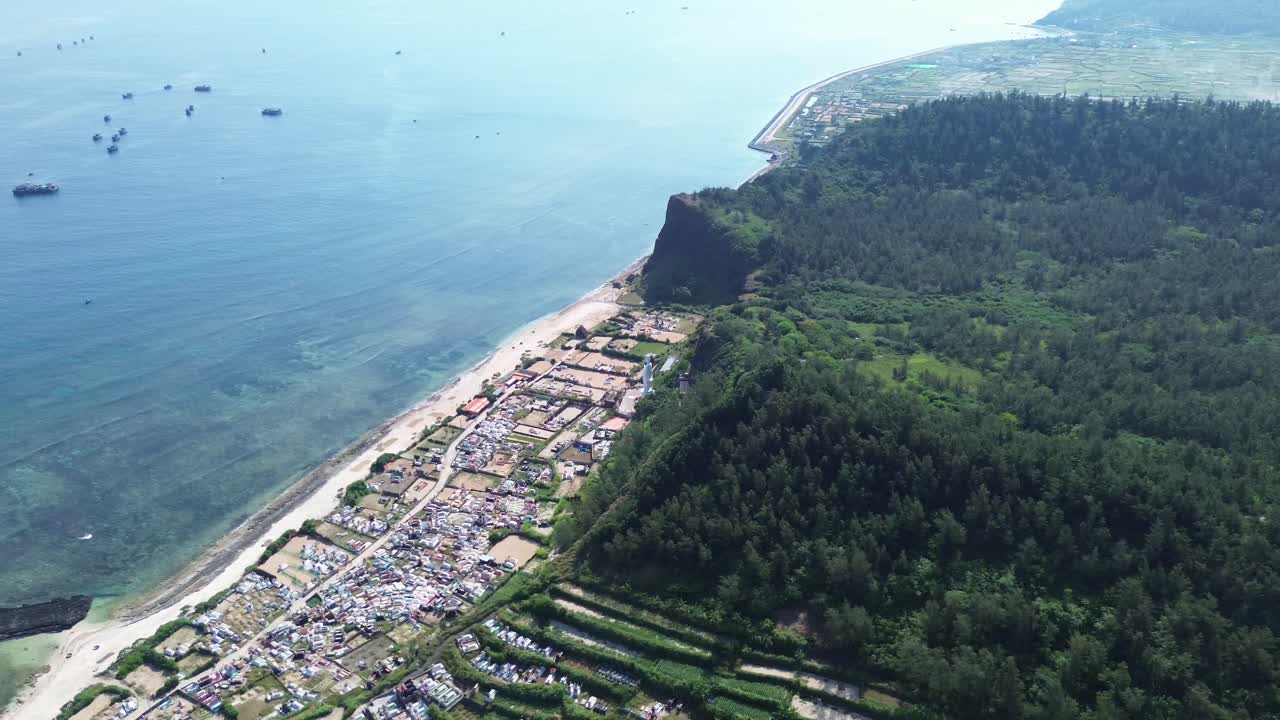 Pan left view of a lush forested area and volcanic formations descending toward the sea in Ly Son