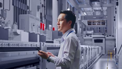 side view of an asian male professional worker standing at pharmaceutical factory, vaccine production facility, observes by looking up then he come to concentrating on the phone and keep on checking