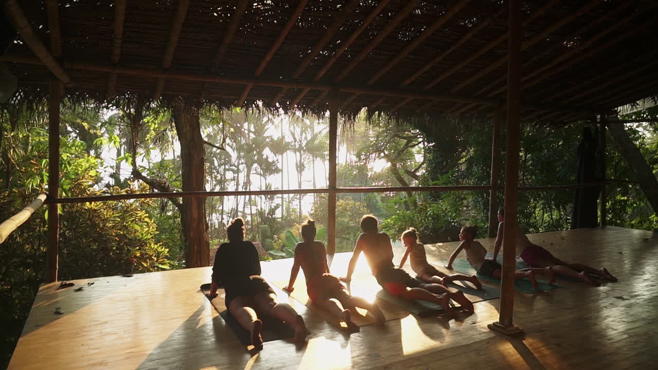 A group of travelers enjoying a sunset meditation and yoga session on a sunny wooden porch overlooking the rainforest and jungle leading out to the beach.