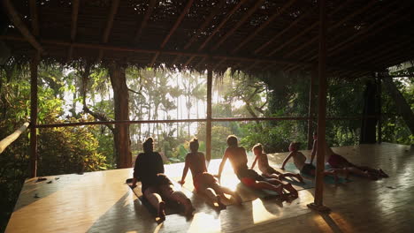 a group of travelers enjoying a sunset meditation and yoga session on a sunny wooden porch overlooking the rainforest and jungle leading out to the beach.