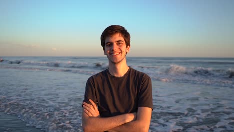 feliz joven de pie en la playa con los brazos cruzados