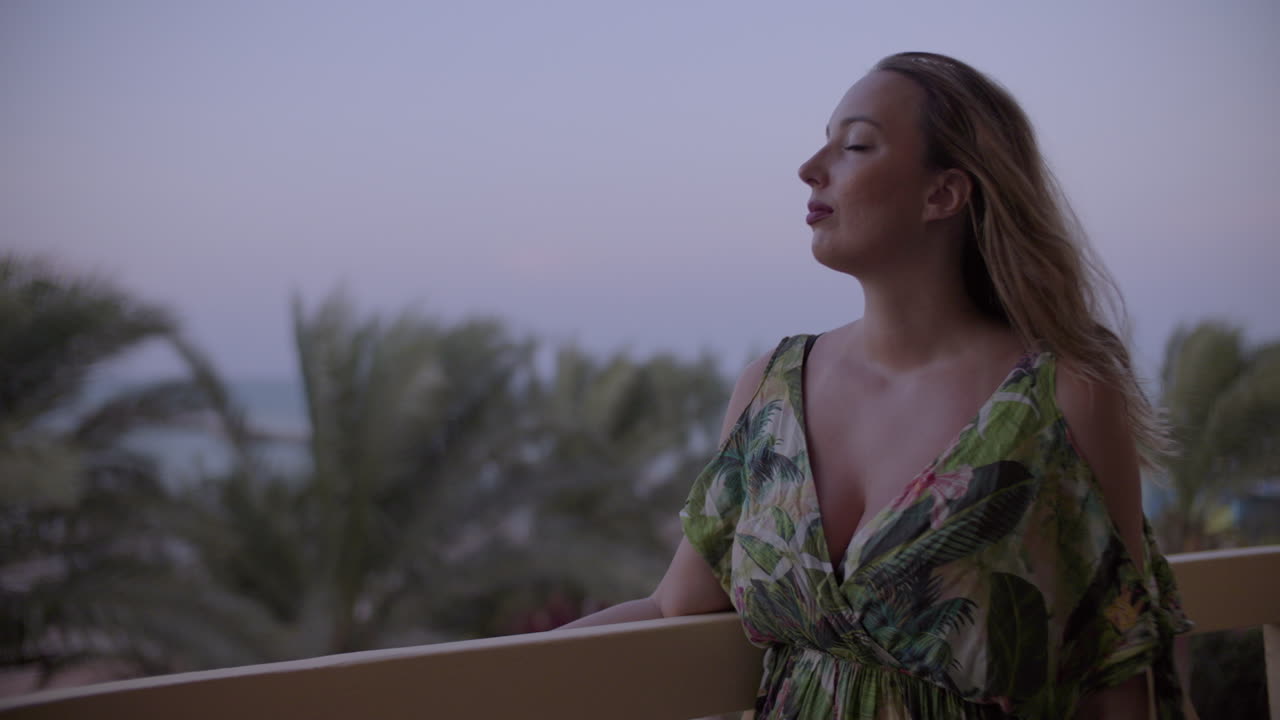 mujer joven en un balcón mirando a lo lejos y disfrutando del viento por la tarde