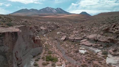 Drone-passing-through-a-little-canyon-on-the-Chilean-desert-with-a-volcano-on-the-background