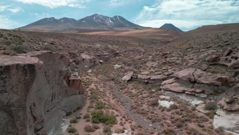 drone pasando por un pequeño cañón en el desierto chileno con un volcán en el fondo