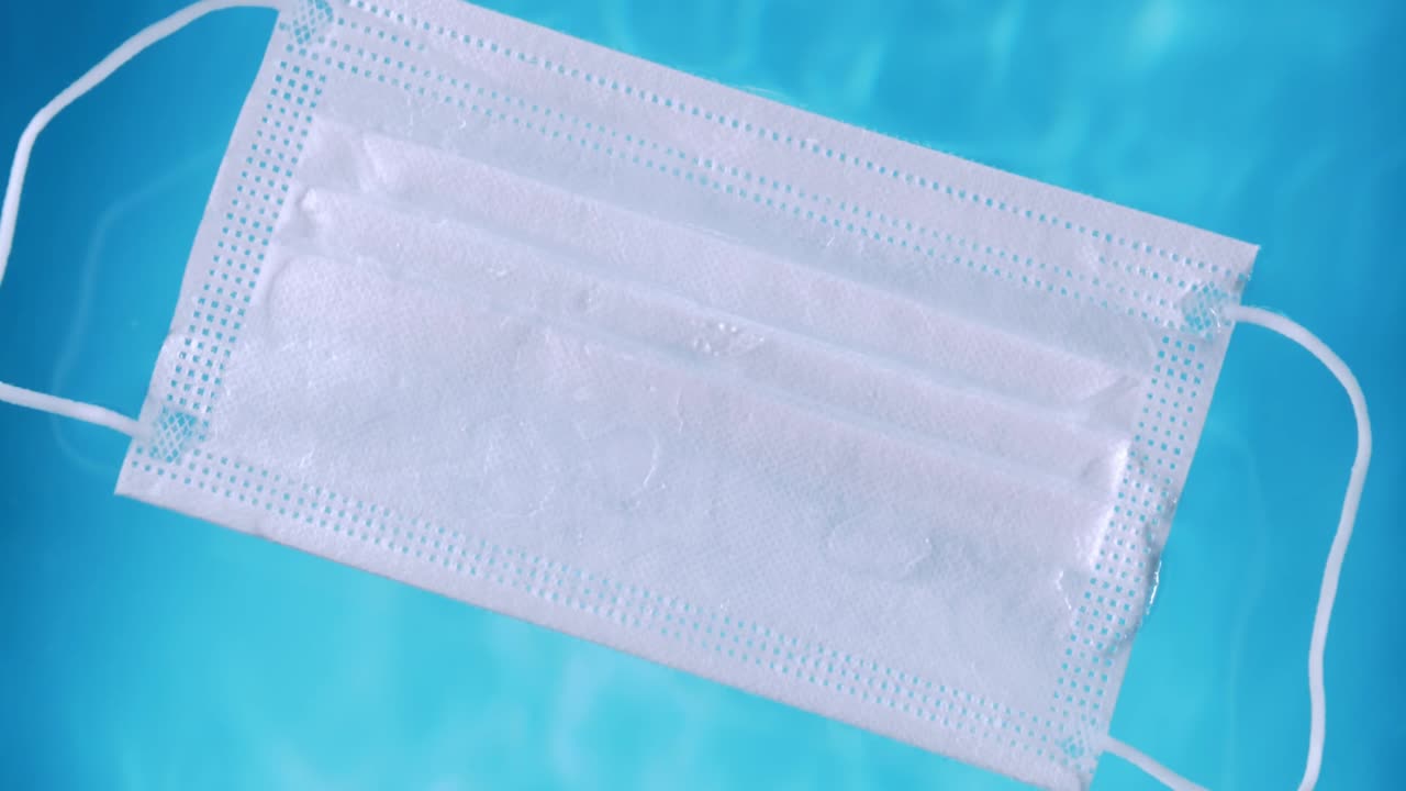 una máscara protectora médica en la superficie del agua contaminación del agua durante la crisis del covid-19 con lazos que se desplaza lentamente en la superficie del agua
